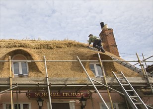 A thatcher completing the re-thatching of a traditional country pub, the Sorrel Horse, Shottisham,