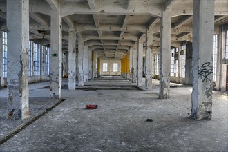 Empty dilapidated factory building, pillars, peeling paint, light entering through broken window