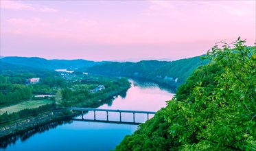 Twilight over a serene river landscape with bridge and mountains, in South Korea