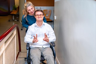Health worker pushing a happy man with down syndrome using wheelchair while he gesturing success