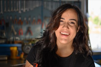 Smiling hispanic female mechanic in workshop standing in front of a workbench, a complete tool