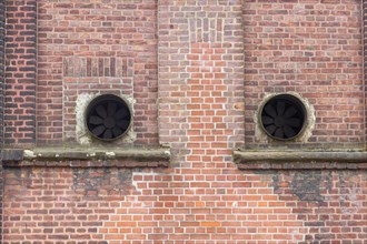 Old brick facade with round ventilation openings in the wall