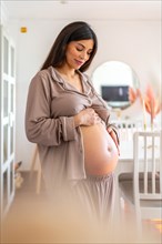 Vertical portrait of a beauty pregnant woman looking and touching her belly at home