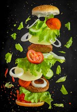 Flying burger, floating ingredients, tomatoes, lettuce, cheese, onion in front of a dark background