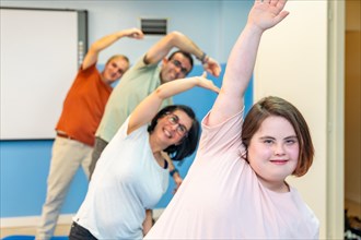 Focus on a woman with down syndrome and a group of people with special needs stretching in the gym