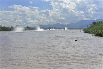 Speedboats create water fountains on a river with cloudy sky in the background, Inle Lake, Myanmar,
