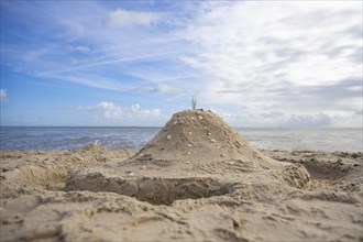 Sandcastle with shells and moat on the beach, in the background sea and blue sky, Schillig,