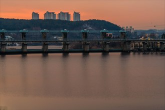 Golden hour sunset illuminating a dam on the river with buildings behind, in South Korea