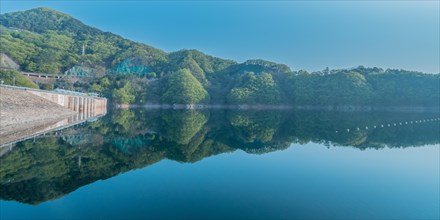 Still morning at a dam with forested hills and perfect reflections in the reservoir, in South Korea