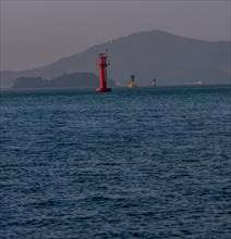 Three small lighthouses in a harbor with small mountains shrouded in fog and mist in the background