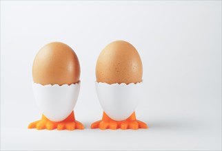 Two fresh eggs in an egg cup in the shape of a chicken on a white background