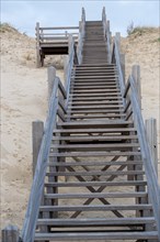 Perspective of a long wooden staircase leading through the dunes