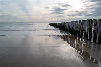 Wooden breakwater on a sandy beach with clouds in the sky at sunset