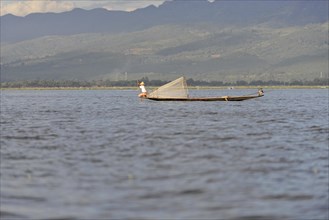 Fisherman in a small boat in the middle of the water, mountains in the background, Inle Lake,