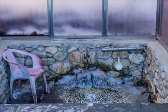A frozen outdoor sink and tap with a pink chair against a frost-covered stone wall, in South Korea