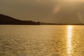 Calm lake reflecting the golden light of the setting sun with a hilly backdrop, in South Korea