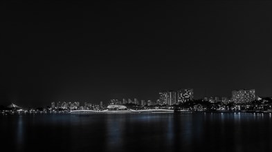 A serene black and white night shot of city skyline reflections on water, in South Korea