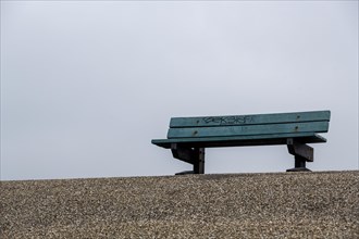 A lonely bench on a pebble beach with a foggy and quiet atmosphere