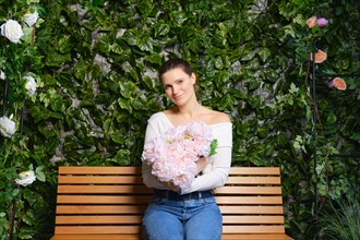 Lovely woman sits on a wooden bench, embracing a bouquet of delicate pink flowers
