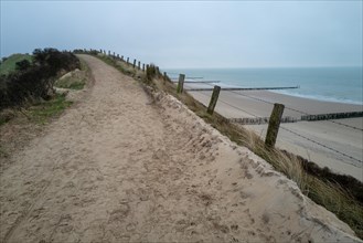 A sandy path winds through the dunes on a calm, cloudy day by the sea