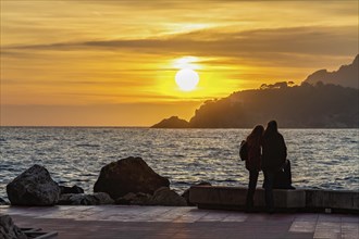 Silhouette of a couple enjoying a sunset by the ocean on a promenade, Peguera, Mallorca