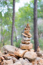 Carefully stacked, slightly red stones form a stone figure, cairn, waymark, marker, sparse pine