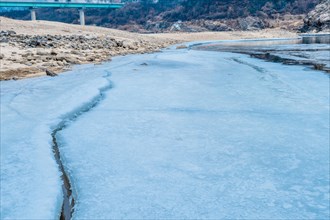 Frozen river leading towards a bridge with icy banks on either side, in South Korea