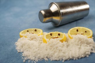 Lemon slices with cloves and cinnamon forming a smiley face on a pile of salt next to a shaker with