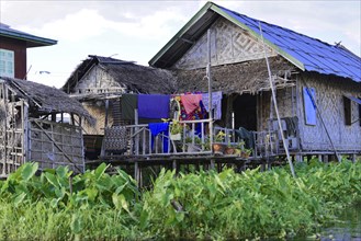 Traditional bamboo hut in a floating village with clothesline under a cloudy sky, Inle Lake,