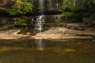 The peacefulness of a waterfall in a dimly lit forest setting with a reflective water surface, in