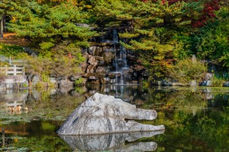 A small waterfall over rocks into a pond, with autumn trees reflecting on the surface, in South