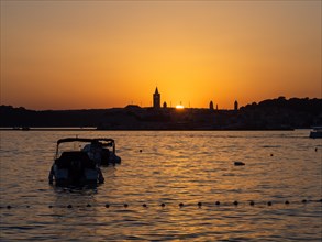 Sunset, silhouette of the church towers of Rab, boats anchoring in a bay, town of Rab, island of
