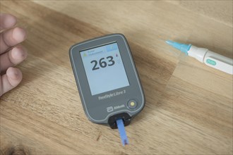 Blood glucose meter with test strips and a drop of blood lies in the centre of a wooden table, high