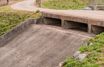 A basic concrete culvert under a pathway in a rural setting with an embankment, in South Korea