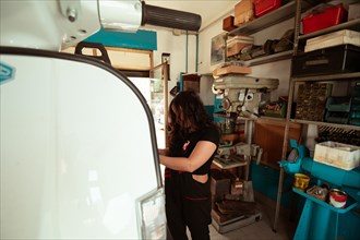 Focused hispanic young sensual long haired brunette woman mechanic inspecting a vintage scooter in