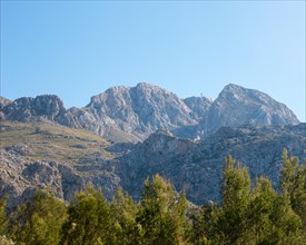 Blue sky over a picturesque, sunny mountain landscape, bare, steep rocky peaks, green trees, pine