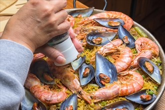 Close-up of a hand seasoning traditional seafood paella with rich colors, typical Spanish cuisine,