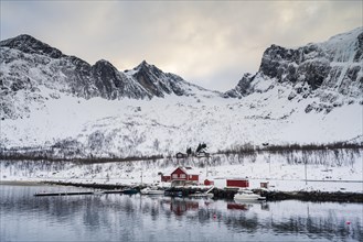 Red boathouse by the fjord, snow-covered mountains, Ersfjorden, Senja Island, Norway, Europe