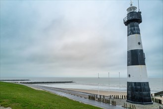 A black and white lighthouse with beach piles and a green area on a cloudy day, Breskens, Zeeland,