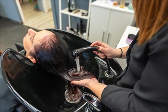 Top view of a female hairdresser rinsing shampoo from a woman's hair at the hair salon