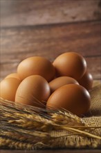 Fresh eggs on a burlap cloth on a wooden table with out-of-focus ears of wheat