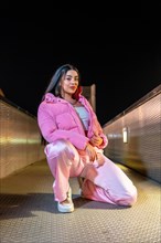 Vertical portrait of a female beauty and young hip hop dancer in pink clothes kneeling outdoors at
