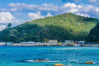 Scenic view of a coastal village by the sea with mountains and blue sky, in South Korea