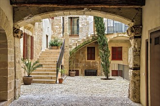 A serene cobblestone courtyard with potted plants and an archway leading to stairs, Palma De
