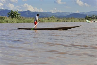 A child stands on a narrow boat on a quiet river, Inle Lake, Myanmar, Asia
