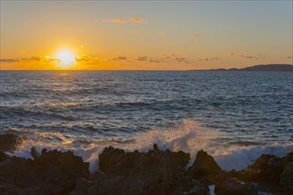 Sunset over the sea with waves breaking on rocks under a partly cloudy sky, Finikounda,