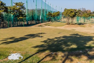 Winter scene at a golf course with shadows on the grass and a net barrier, in South Korea