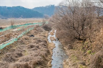 Overcast skies over a barren winter landscape with a meandering stream, in South Korea
