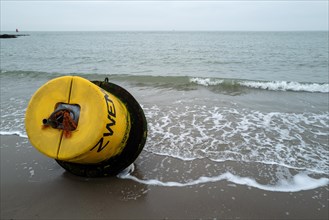 Yellow buoy on a sandy beach with waves in the background on a cloudy day, Westkapelle, Zeeland,