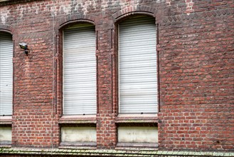Three evenly spaced windows with closed white shutters in a red brick wall